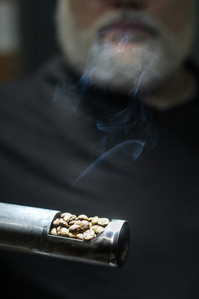 Steve holding up some coffee mid roasting process. The coffee has smoke coming off of it and steves face is blurred in the background