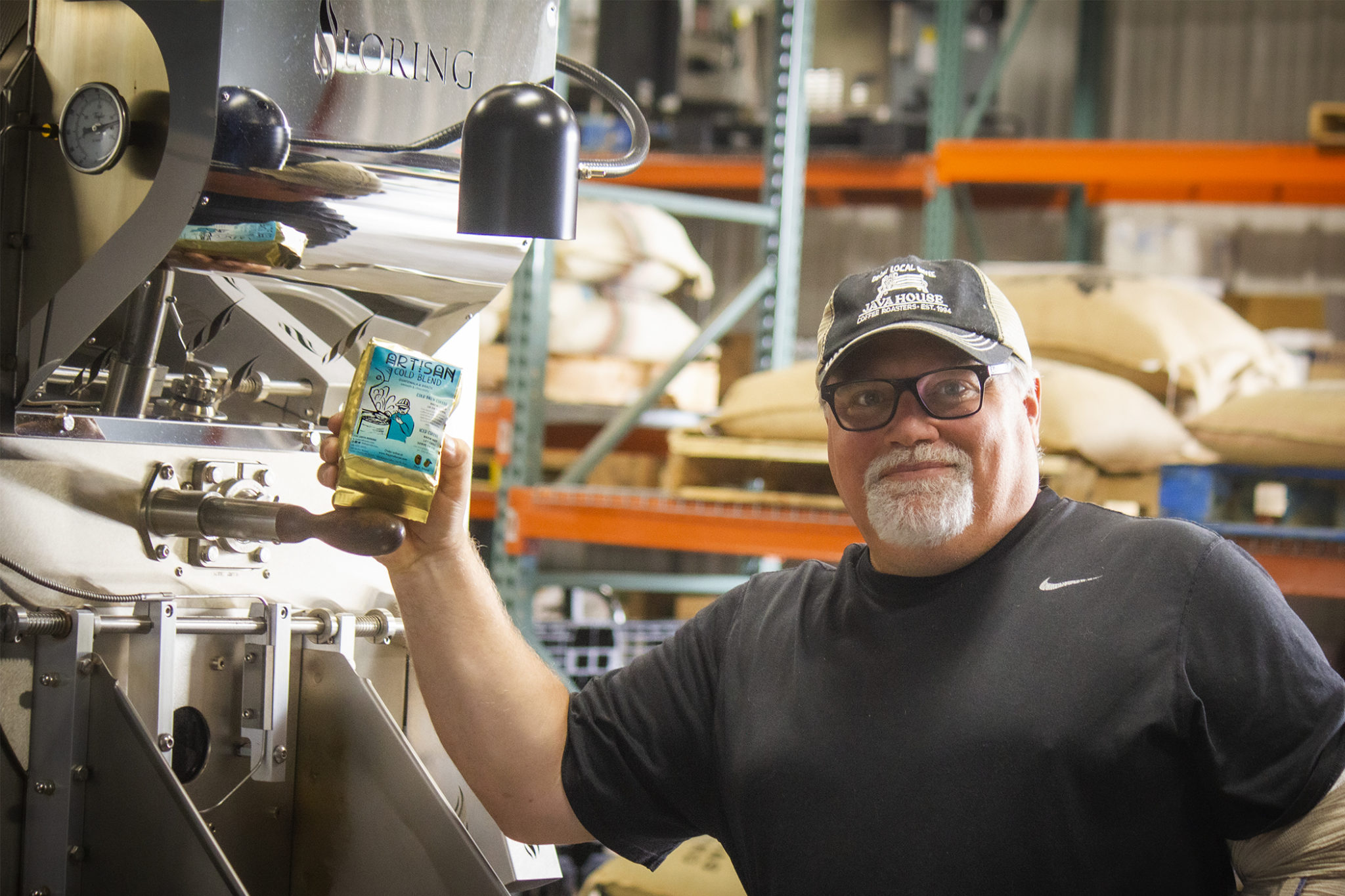 Steve Harris standing in front of our stainless steel roaster, holding a bag of artisan cold blend beans